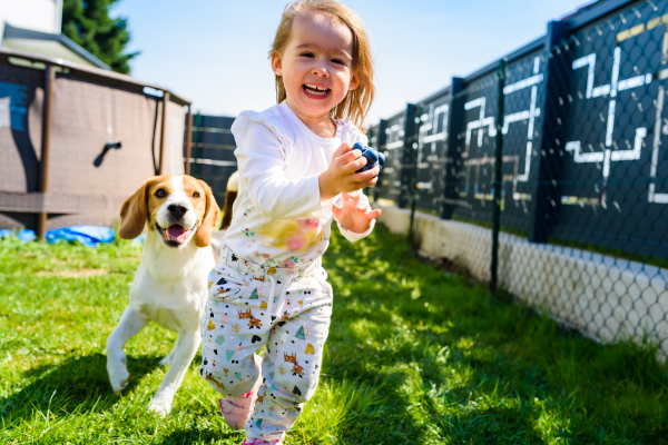 Puppy running with child in a fenced in yard. 